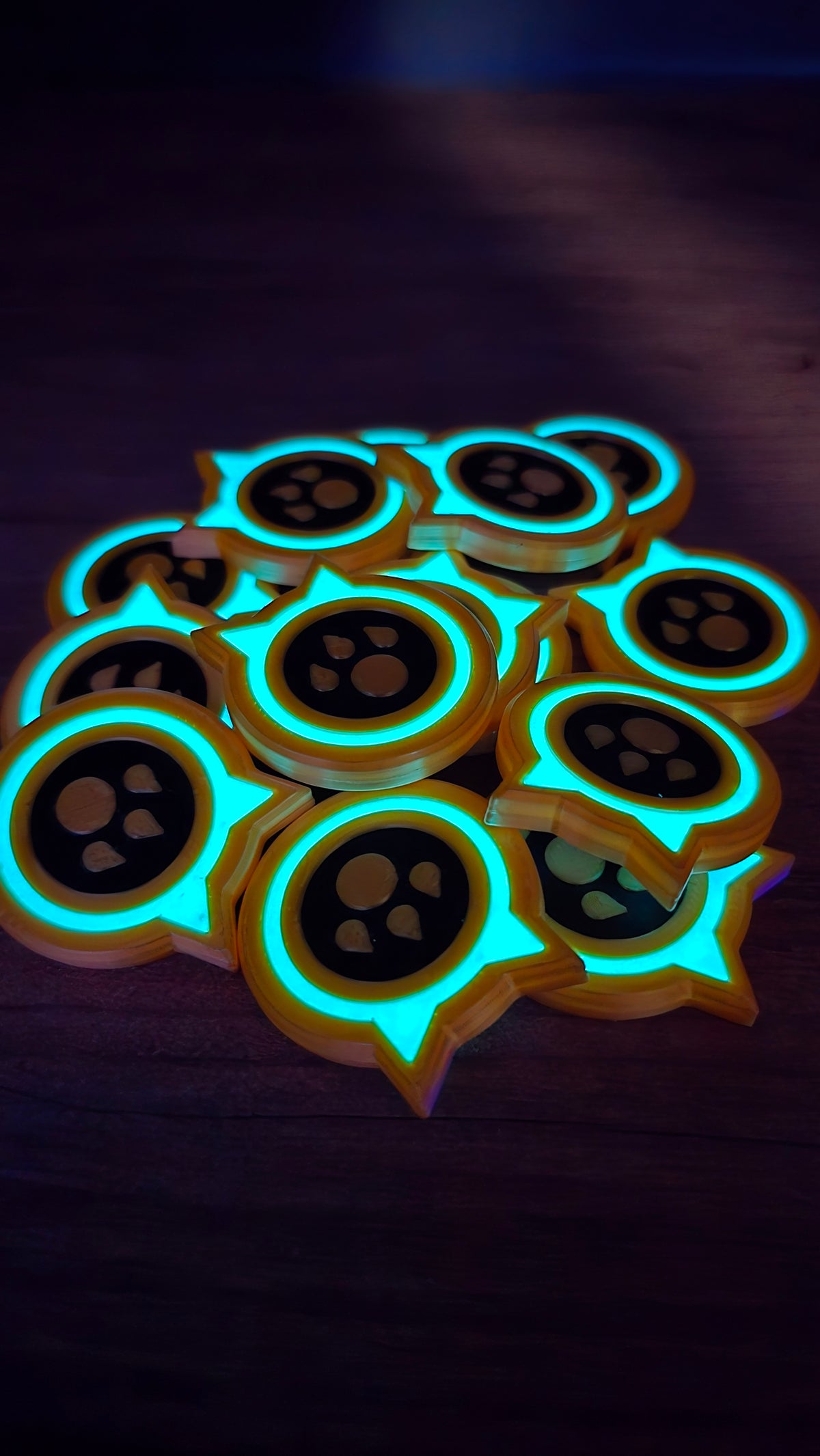 Pile of glow-in-the-dark Palworld-inspired dog coin replicas with turquoise glowing rings and paw-print centers on a dark tabletop.