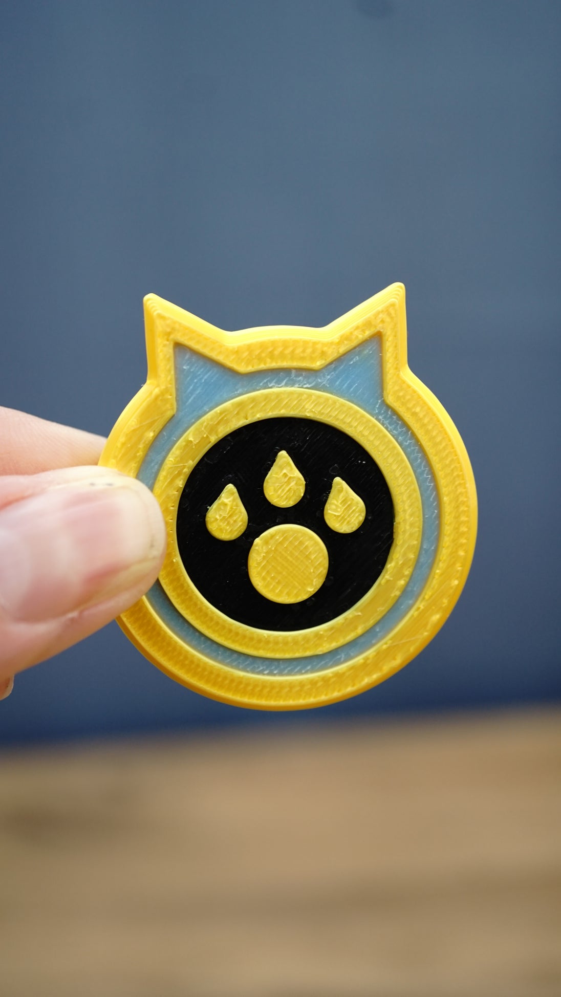 Palworld Dog Coin replica held between fingers to demonstrate its compact 4cm size and detailed yellow, light blue and black design.