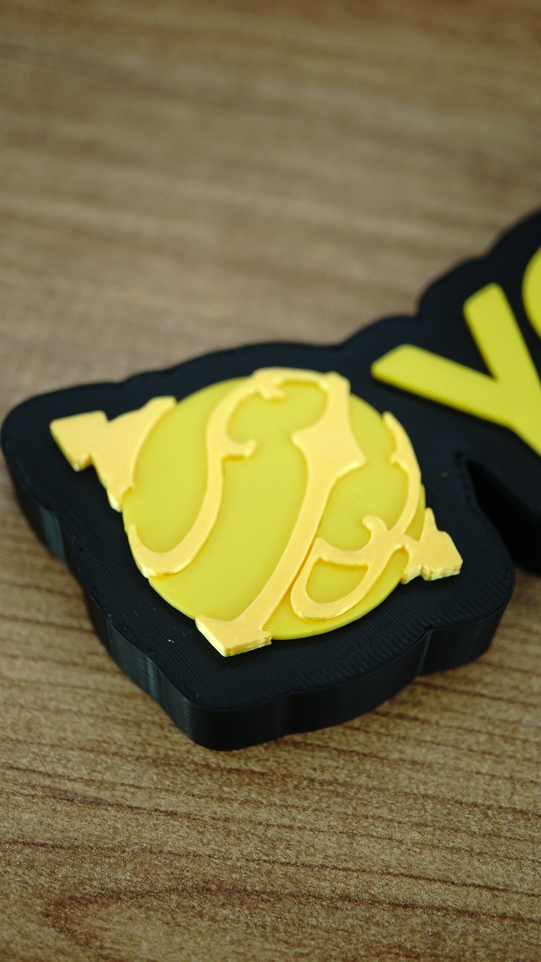 Close-up of the yellow Sphere emblem on a personalised Palworld nameplate, showing the layered decorative detail beside matching yellow lettering.