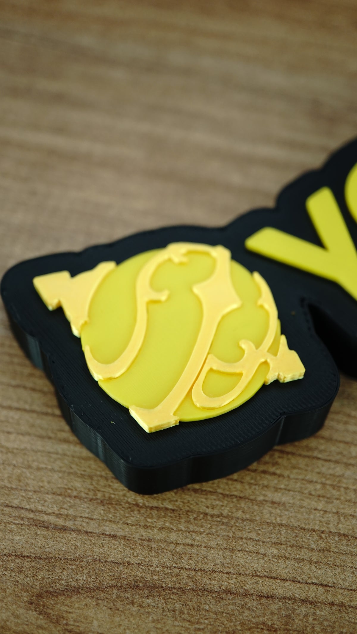 Close-up of the yellow Sphere emblem on a personalised Palworld nameplate, showing the layered decorative detail beside matching yellow lettering.