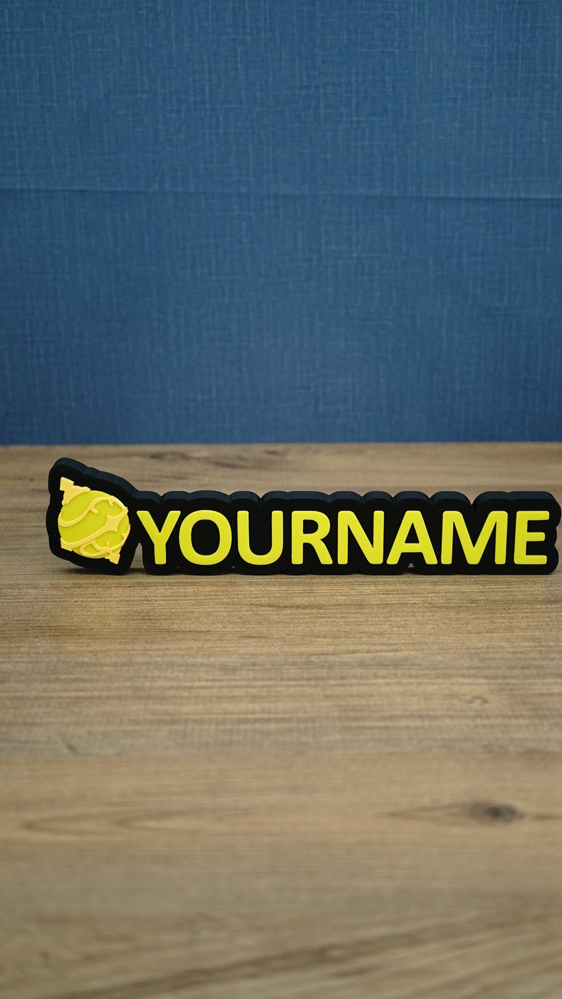 Personalised Palworld Sphere nameplate in yellow on a black base, displayed front-on on a wooden desk as custom gamer room décor with YOURNAME text.
