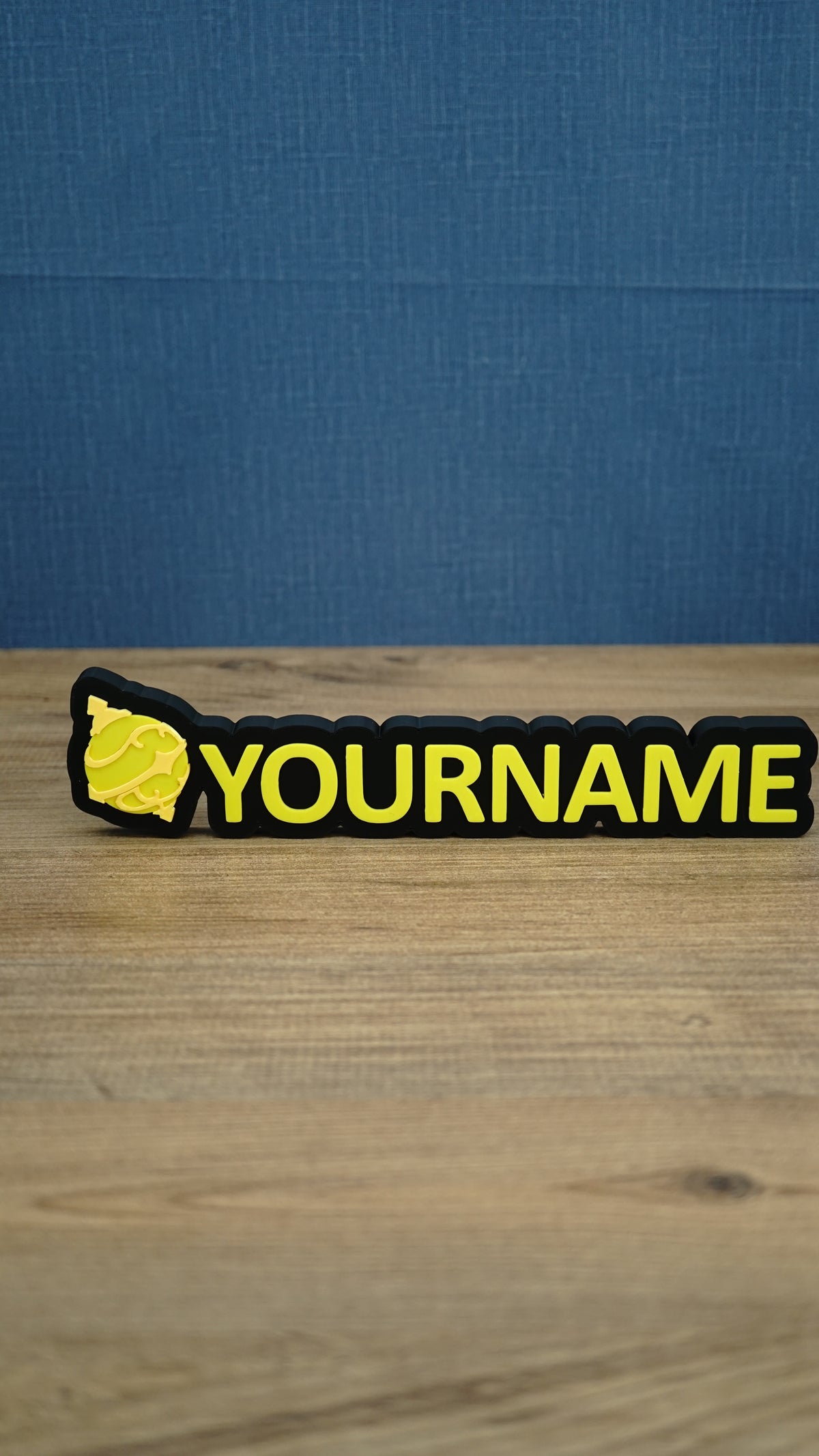 Personalised Palworld Sphere nameplate in yellow on a black base, displayed front-on on a wooden desk as custom gamer room décor with YOURNAME text.