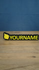 Personalised Palworld Sphere nameplate in yellow on a black base, displayed front-on on a wooden desk as custom gamer room décor with YOURNAME text.