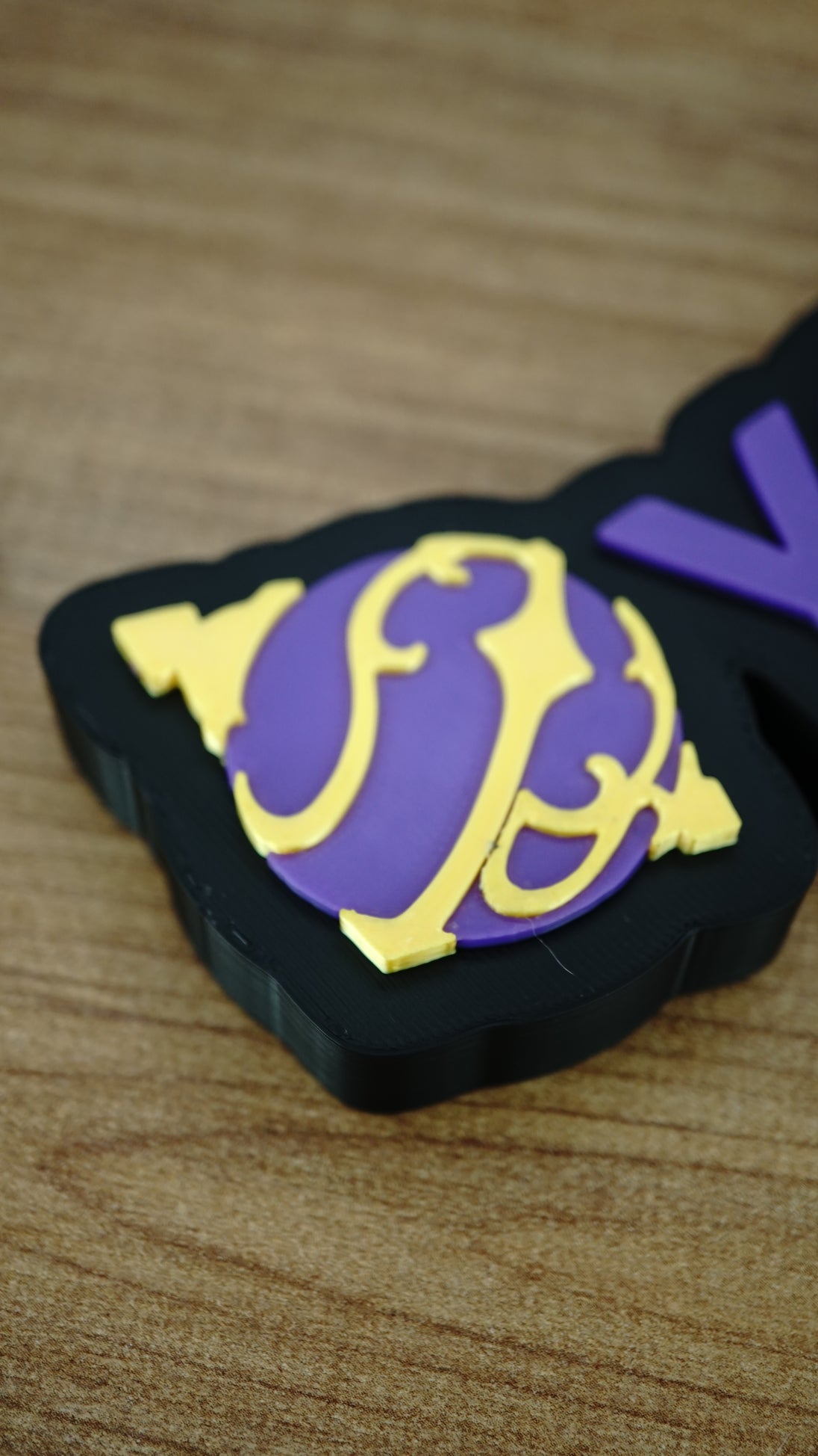 Close-up of the purple and yellow Sphere emblem on a personalised Palworld nameplate, with matching purple lettering on a black display base.