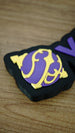 Close-up of the purple and yellow Sphere emblem on a personalised Palworld nameplate, with matching purple lettering on a black display base.