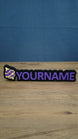 Personalised Palworld Sphere nameplate in purple and yellow on a black base, shown front-on with raised custom YOURNAME lettering for a gaming setup.