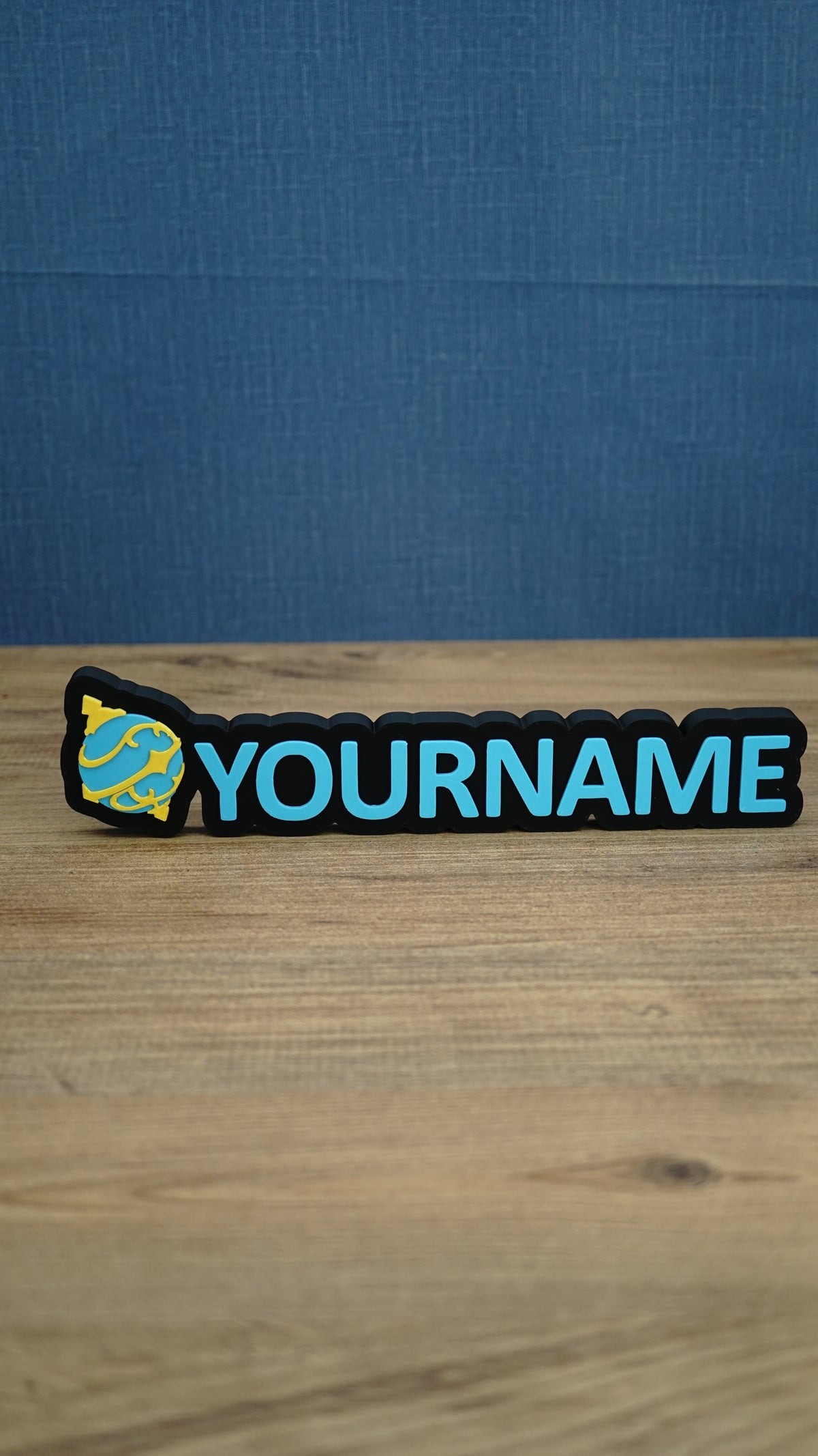 Personalised Palworld Sphere nameplate in blue and yellow on a black base, displayed front-on with custom YOURNAME lettering on a wooden desk.