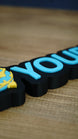 Close-up of raised blue YOURNAME lettering on a personalised Palworld Sphere desk nameplate, showing the smooth face and black outlined base.