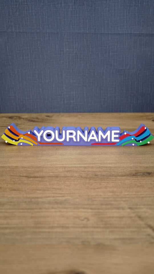 Front view of a personalized Palia Prismatic Pride nameplate with white lettering, a purple base, rainbow flourishes, and small white accents.