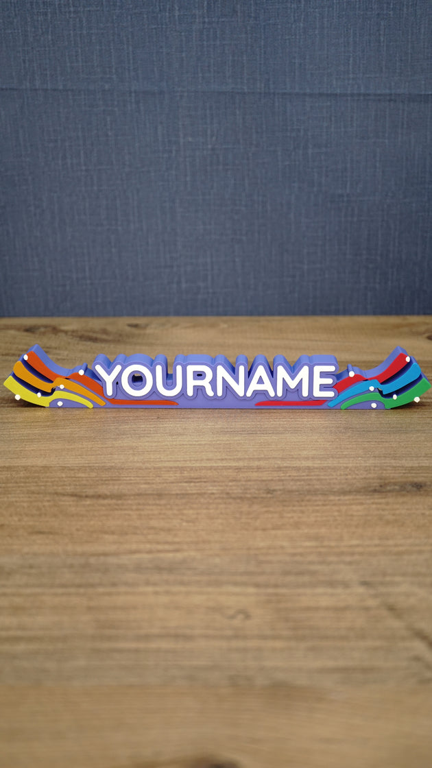 Front view of a personalized Palia Prismatic Pride nameplate with white lettering, a purple base, rainbow flourishes, and small white accents.