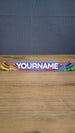 Front view of a personalized Palia Prismatic Pride nameplate with white lettering, a purple base, rainbow flourishes, and small white accents.