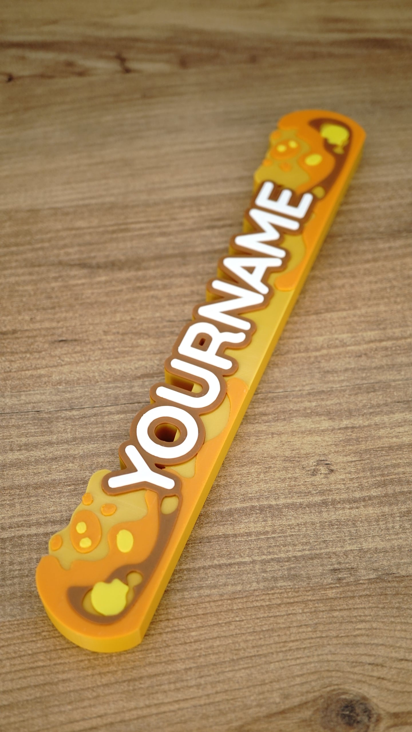 Full diagonal view of a 25 cm personalized Palia nameplate featuring Royal Amber-inspired orange, yellow and brown details with custom white text.