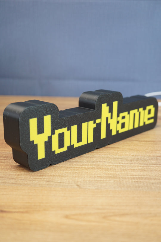 Angled view of a personalized YourName LED desk sign featuring RuneScape-style yellow lettering and a bold black frame.