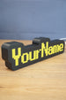 Angled view of a personalized YourName LED desk sign featuring RuneScape-style yellow lettering and a bold black frame.