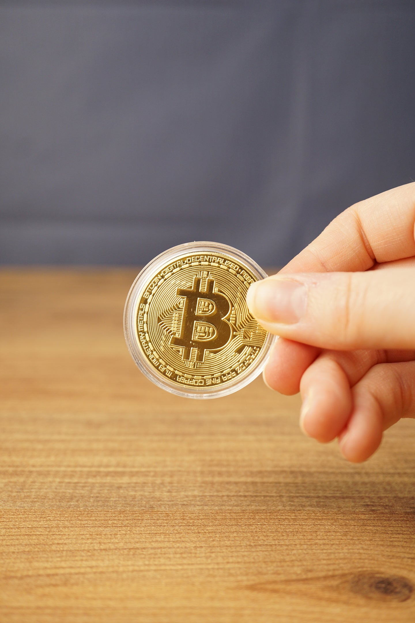 Hand holding a gold physical Bitcoin replica in a clear protective case, showing the raised Bitcoin logo and engraved coin details.