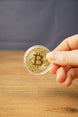 Hand holding a gold physical Bitcoin replica in a clear protective case, showing the raised Bitcoin logo and engraved coin details.