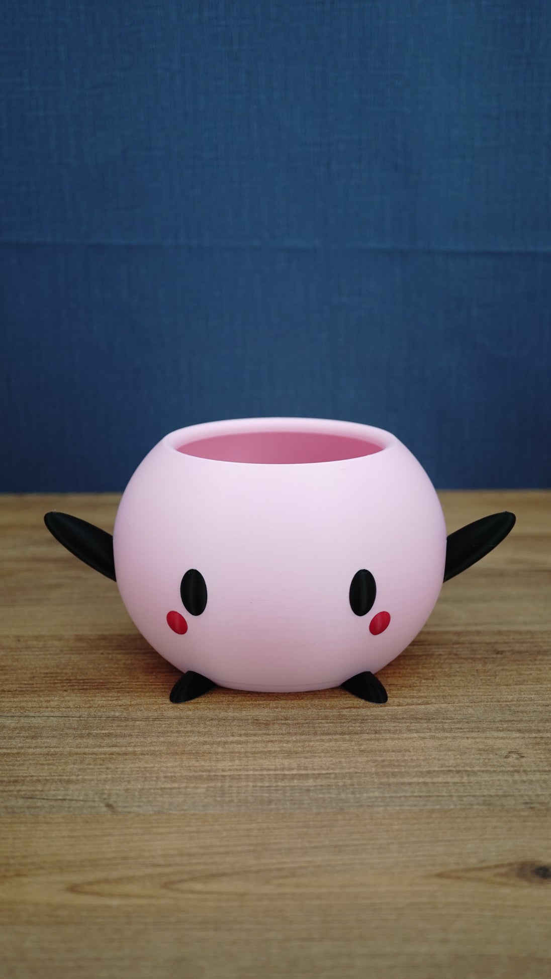 Pink Stardew Valley-inspired Junimo planter pot with black arms and feet, oval black eyes, and red cheek details.