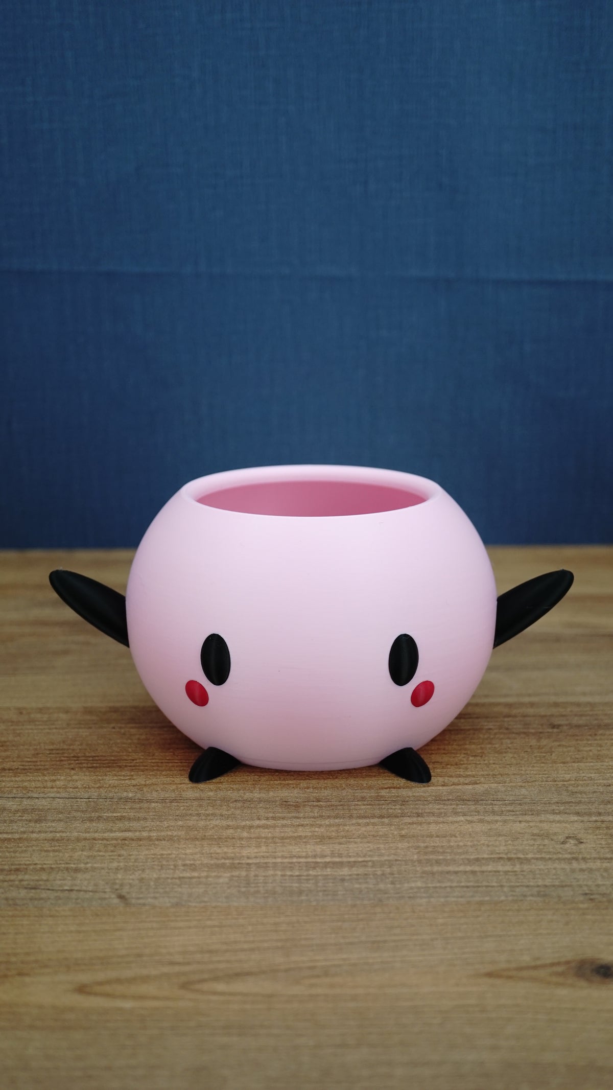 Pink Stardew Valley-inspired Junimo planter pot with black arms and feet, oval black eyes, and red cheek details.