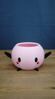 Pink Stardew Valley-inspired Junimo planter pot with black arms and feet, oval black eyes, and red cheek details.