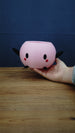 Hand holding a large pink Junimo-inspired planter pot, showing its round open-top design, black arms and feet, and red cheeks.