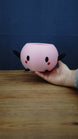 Hand holding a large pink Junimo-inspired planter pot, showing its round open-top design, black arms and feet, and red cheeks.