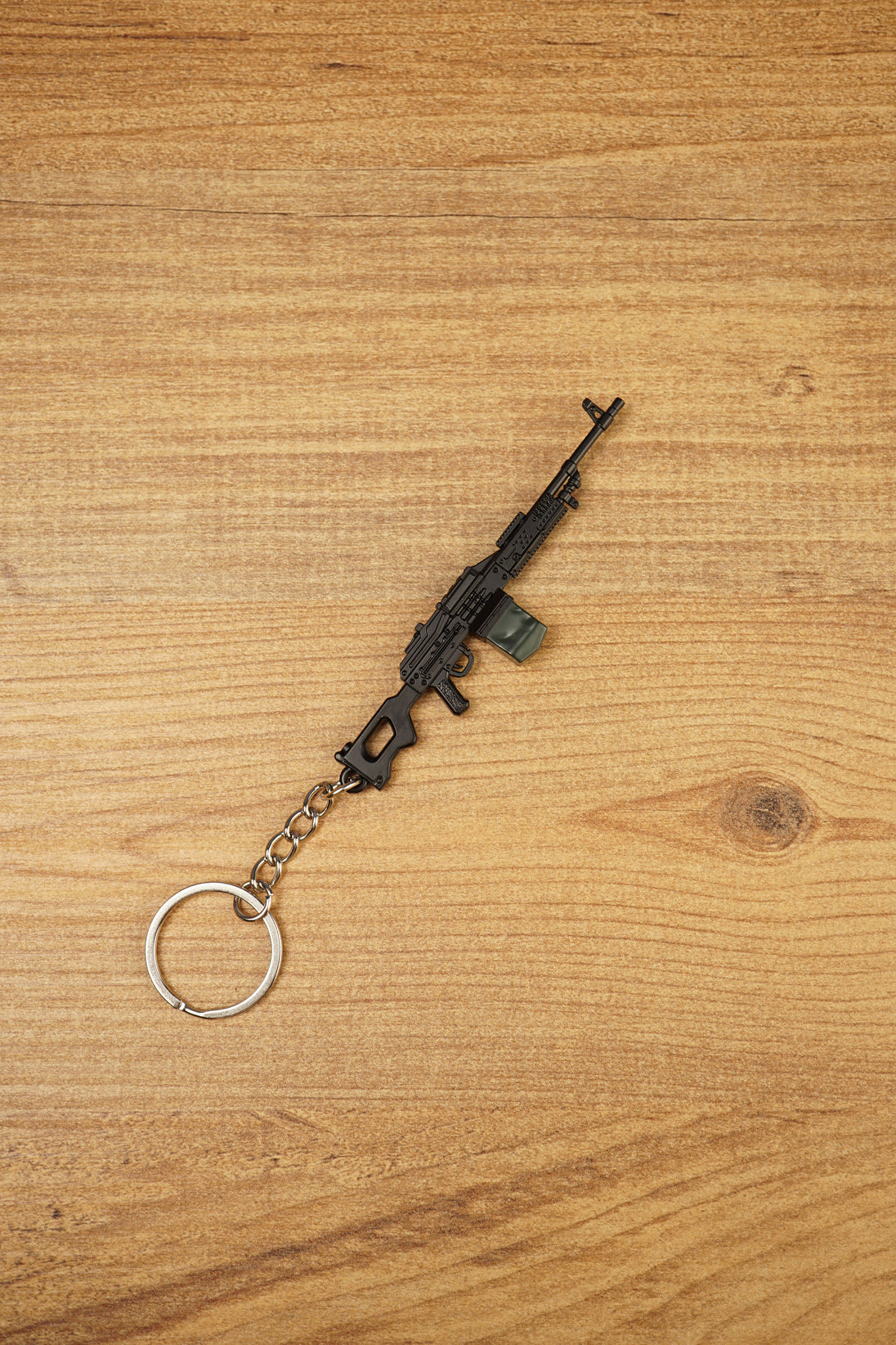 Angled PKM metal rifle keychain on a wooden background, ideal as a tactical shooter accessory, bag charm or gamer collectible