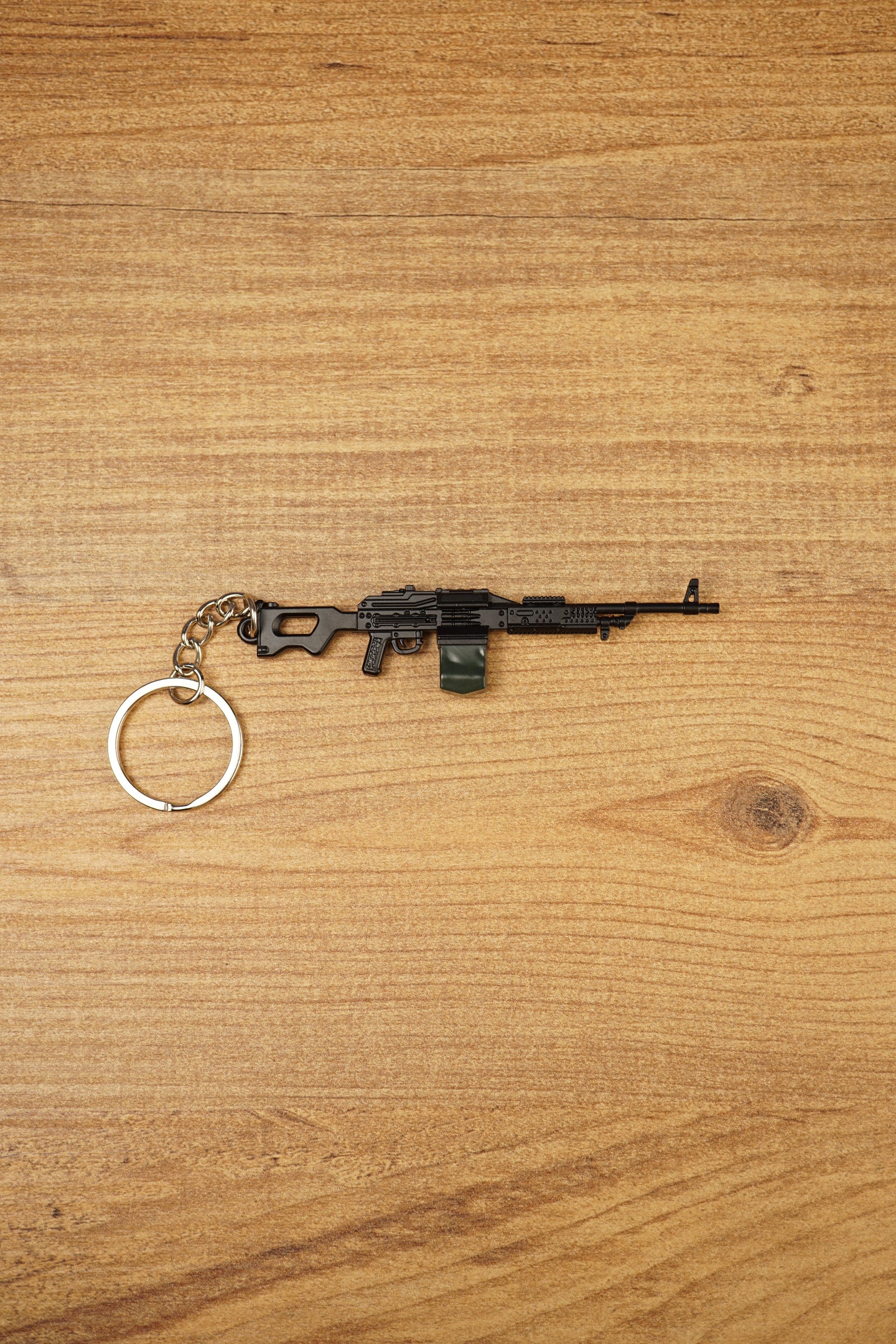 PKM rifle keyring laid flat on a wooden surface, showing the full metal LMG design with chain and key ring for FPS gamer gift use