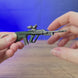 AUG rifle metal gun keyring shown being held and rotated by hand, designed as a miniature rifle-inspired gamer accessory or keychain.