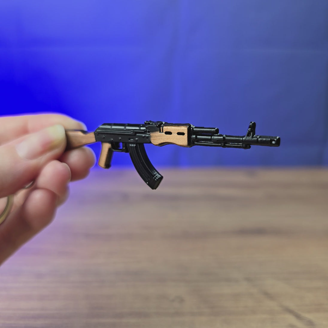 AK-74 rifle keyring shown being held and rotated by hand, designed as a miniature rifle-inspired gamer accessory or keychain.