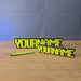 Personalised glow-in-the-dark RuneScape-style nameplate shown being held and displayed, featuring custom OSRS-inspired lettering for gaming desks, shelves, or display setups.