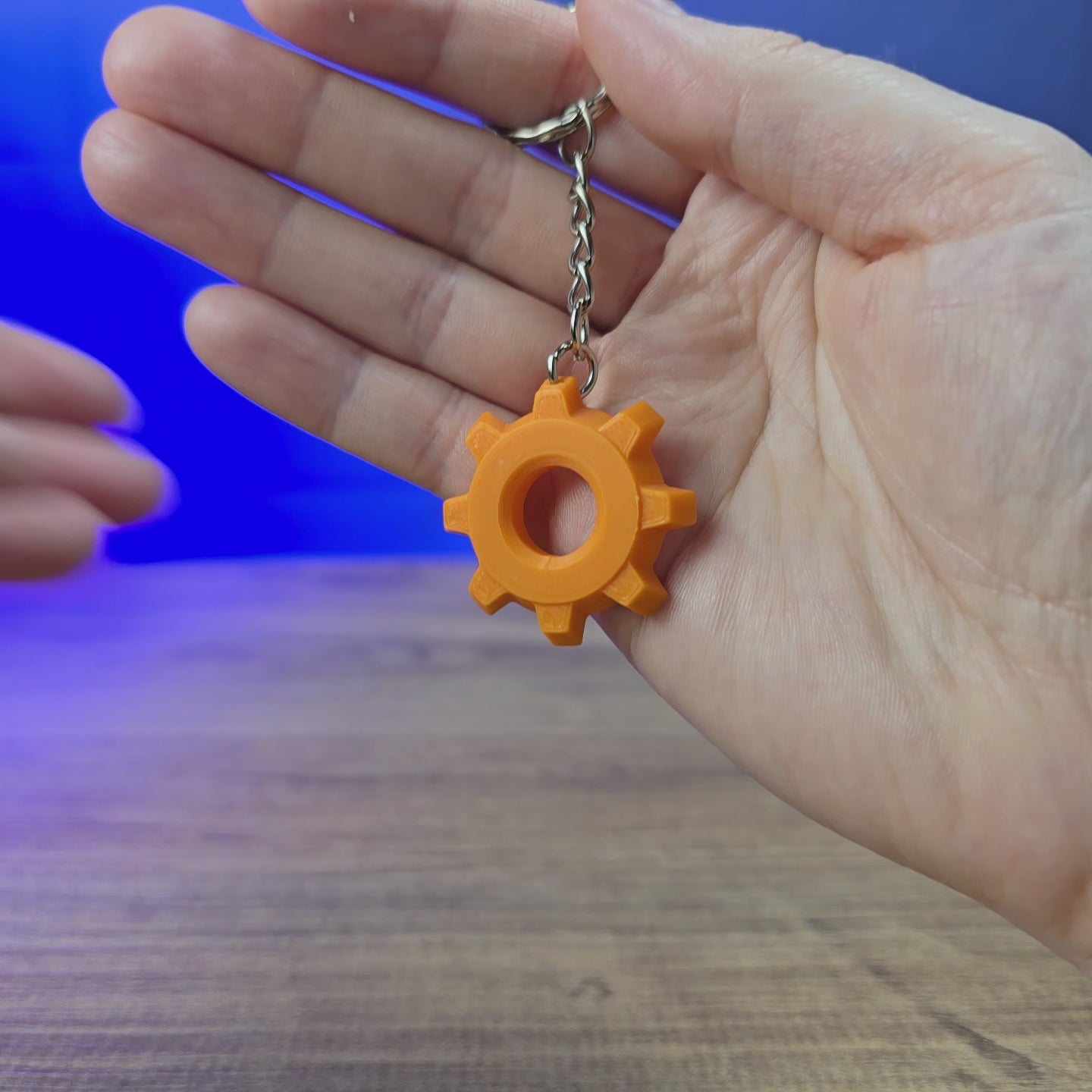3D-printed Factorio cog keyring with a gear-shaped design and keychain loop, shown being held and rotated by hand.
