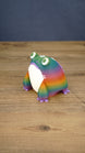 Angled view of a rainbow Frogbert plush figure showing its colorful striped body, white belly, purple feet, and 3D printed texture.