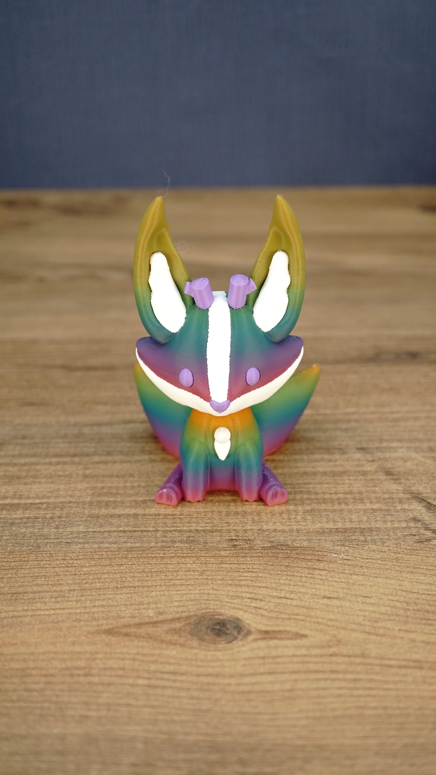 Front view of a rainbow Kitsuu figure with tall ears, white face markings, purple details, and a colorful gradient body.