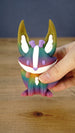 Close-up of a rainbow Kitsuu figure being held, showing the white face stripe, purple nose, tall ears, and colorful 3D printed texture.