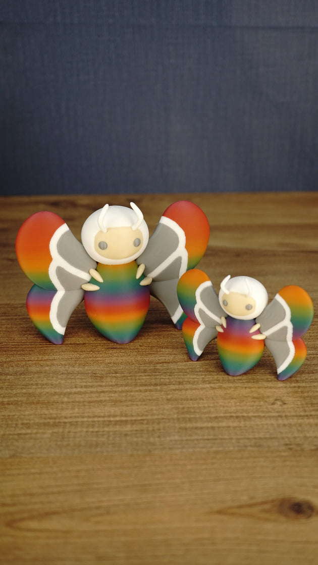 Large 12 cm and small 8 cm Rainbow-Tipped Butterfly Plush figures inspired by Palia, shown together with rainbow bodies and detailed grey wings.