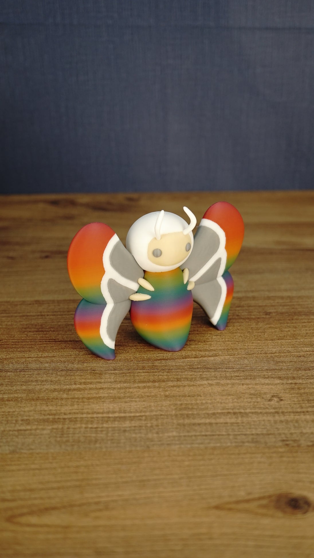 Angled side view of the Palia-inspired Rainbow-Tipped Butterfly figure showing its colourful body, layered wings, antennae and small beige legs.