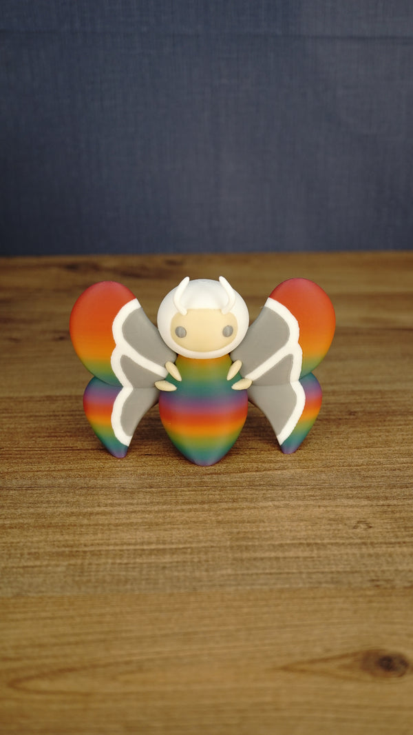 Front view of the Rainbow-Tipped Butterfly Plush figure with a rainbow body, grey and white wings, beige face and curved white antennae