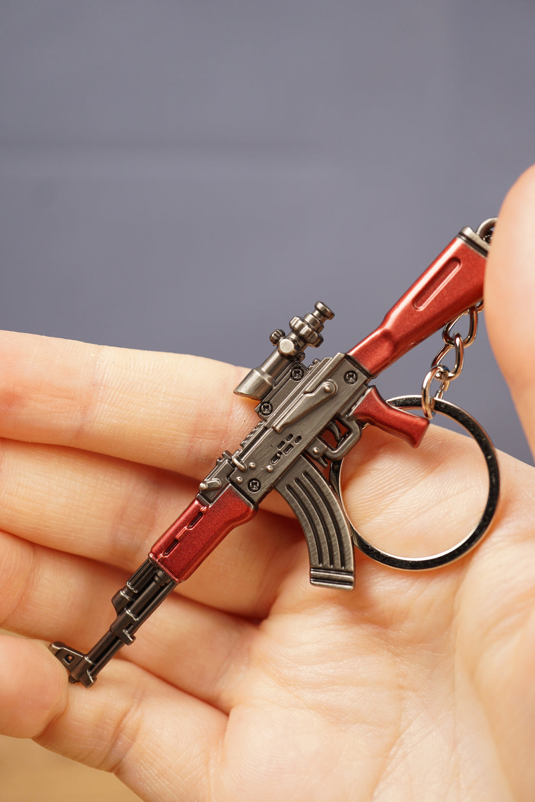 Detailed red AKM-style rifle keyring held in hand with key loop attached, collectible accessory for airsoft and tactical gaming fans