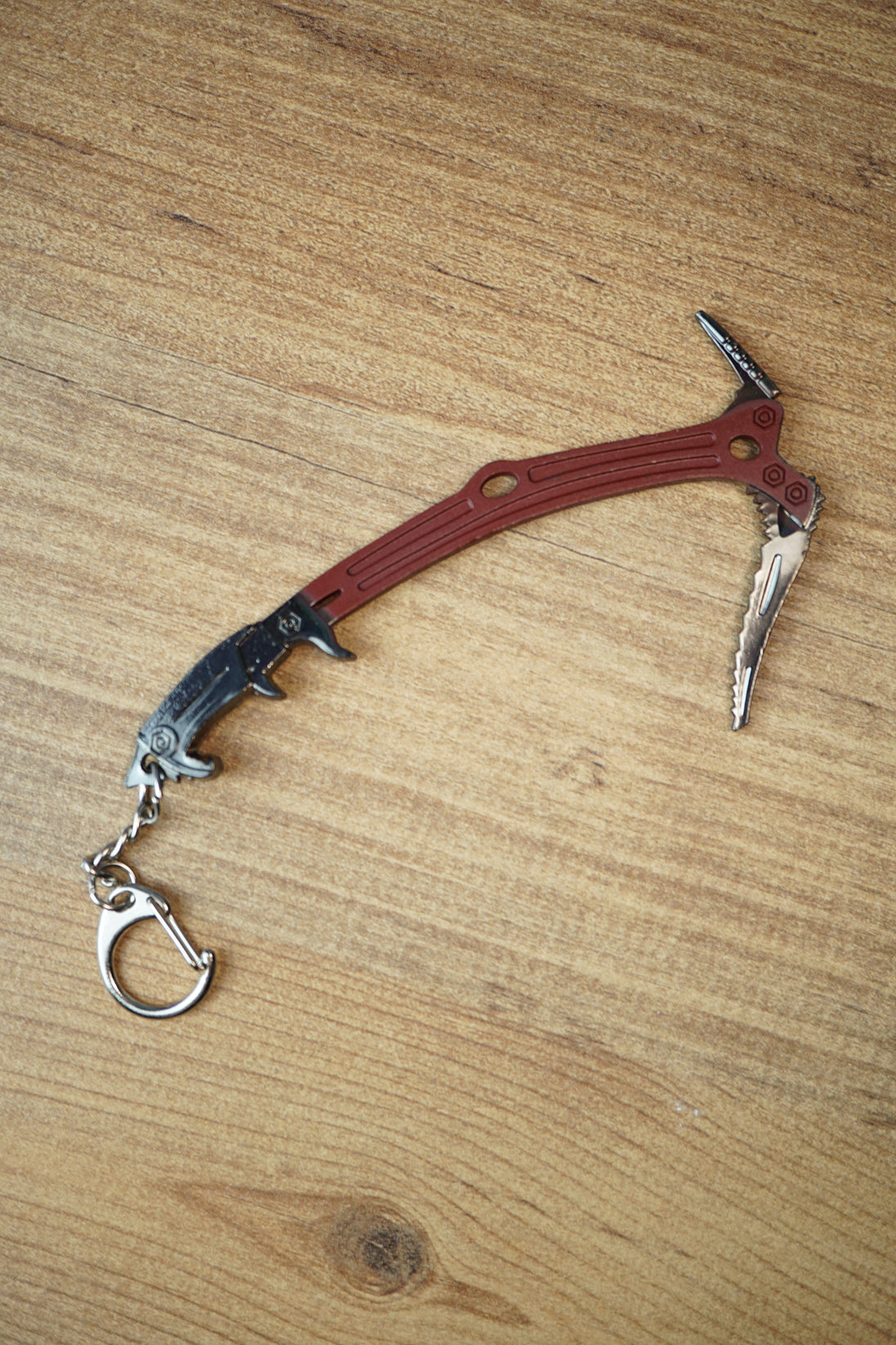 Full Red Rebel ice pick keyring replica displayed on a wooden tabletop, showing the curved red handle, black grip, silver pick, and attached keyring.