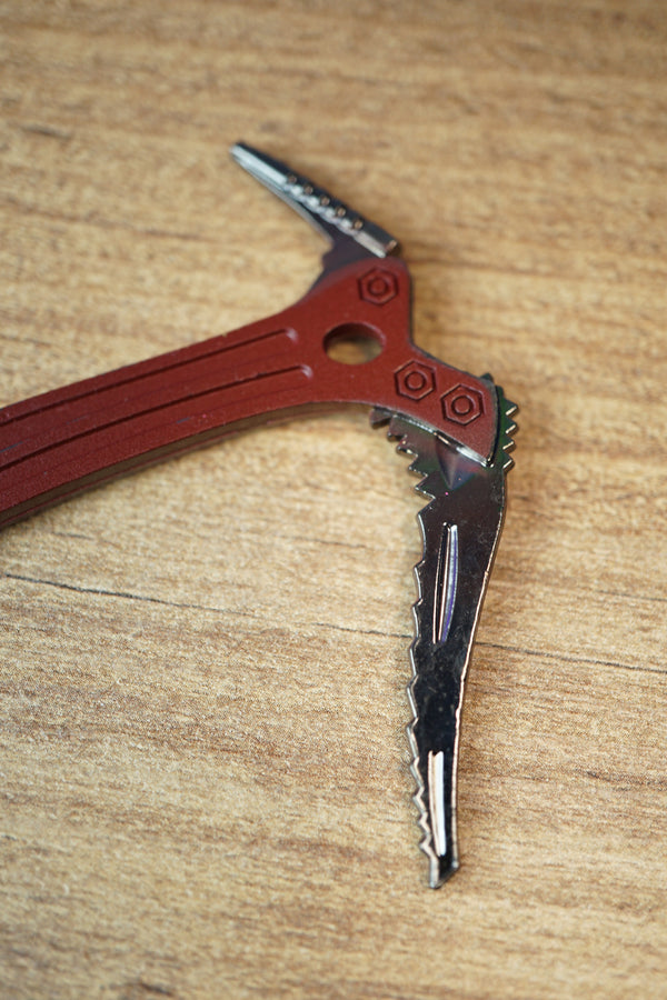 Close-up of the Red Rebel ice pick keyring replica head, featuring red detailing, silver pick edge, bolt accents, and textured tabletop background.