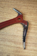 Close-up of the Red Rebel ice pick keyring replica head, featuring red detailing, silver pick edge, bolt accents, and textured tabletop background.