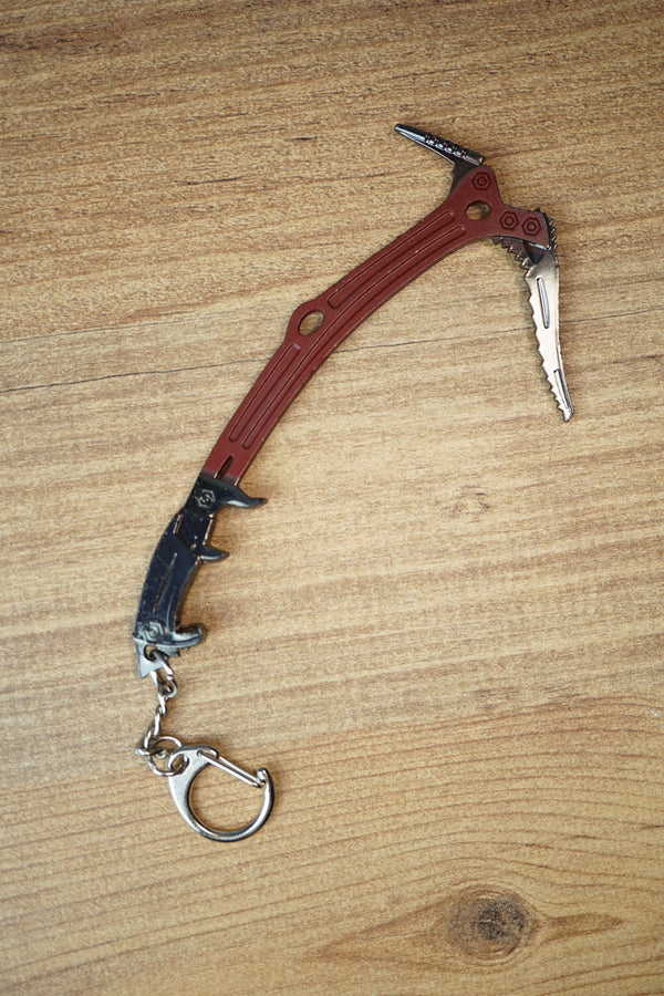 Red Rebel ice pick keyring replica inspired by Tarkov, shown flat on a wooden surface with red handle, black grip, silver pick, and keychain clip.