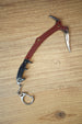 Red Rebel ice pick keyring replica inspired by Tarkov, shown flat on a wooden surface with red handle, black grip, silver pick, and keychain clip.