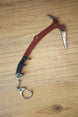 Red Rebel ice pick keyring replica inspired by Tarkov, shown flat on a wooden surface with red handle, black grip, silver pick, and keychain clip.