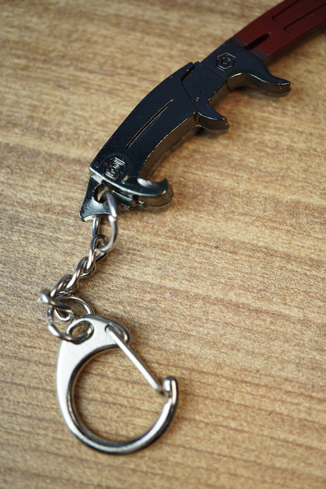 Detailed view of the Red Rebel ice pick keyring replica handle with black grip, silver keychain clip, and metal chain on a wood grain surface.