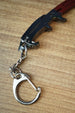 Detailed view of the Red Rebel ice pick keyring replica handle with black grip, silver keychain clip, and metal chain on a wood grain surface.