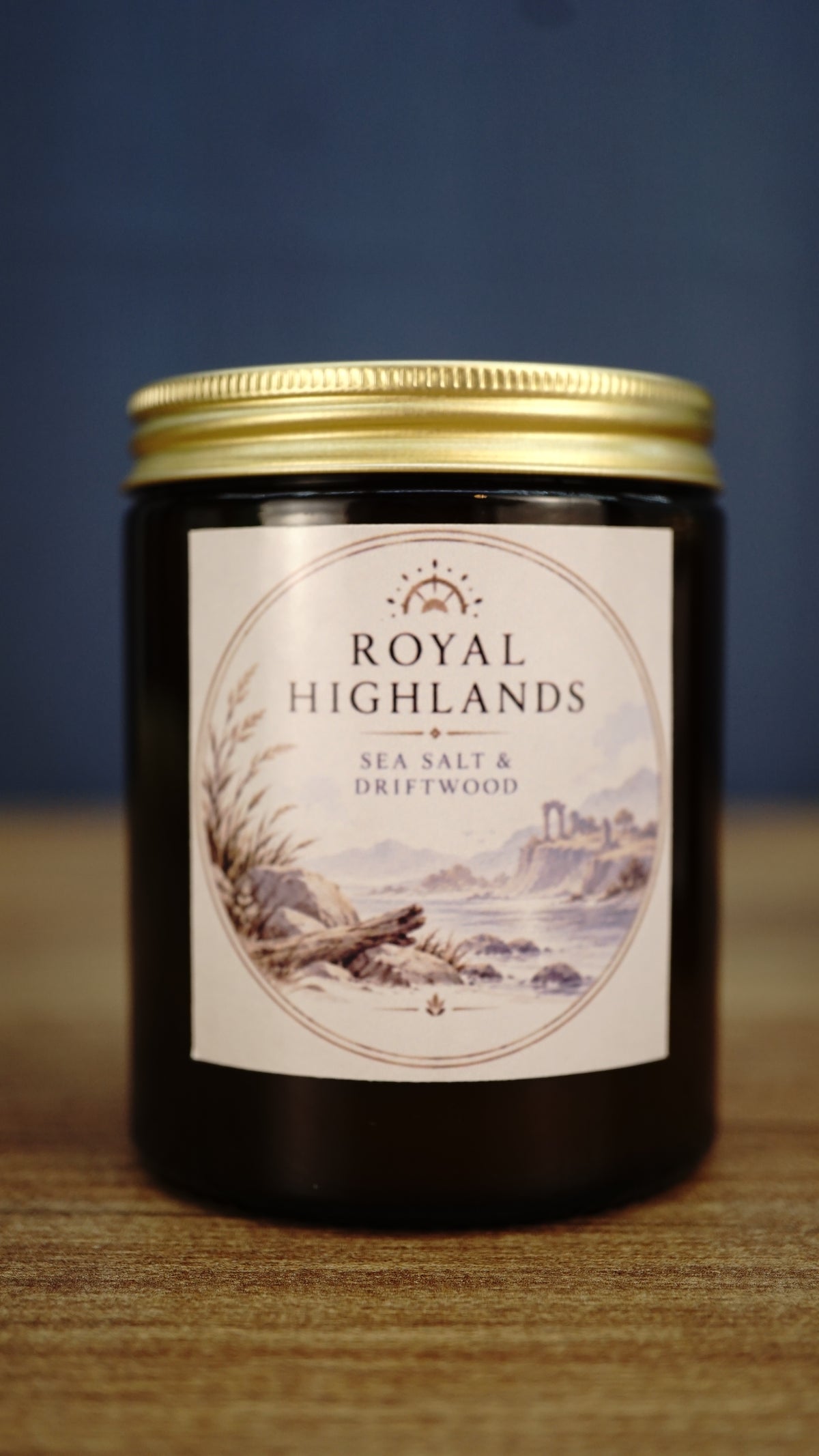 Royal Highlands vegan soy wax candle in an amber glass jar with gold lid, featuring a fresh sea salt and driftwood coastal fragrance.