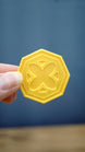 4cm RuneScape inspired gold coin held between fingers to show its size, detailed octagonal shape and raised OSRS-style coin design