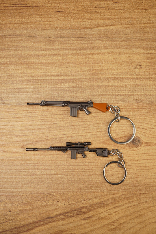 SA58 FAL battle rifle keychains in base and modded styles on a wooden surface, showing metal keyrings and detailed gunmetal finishes