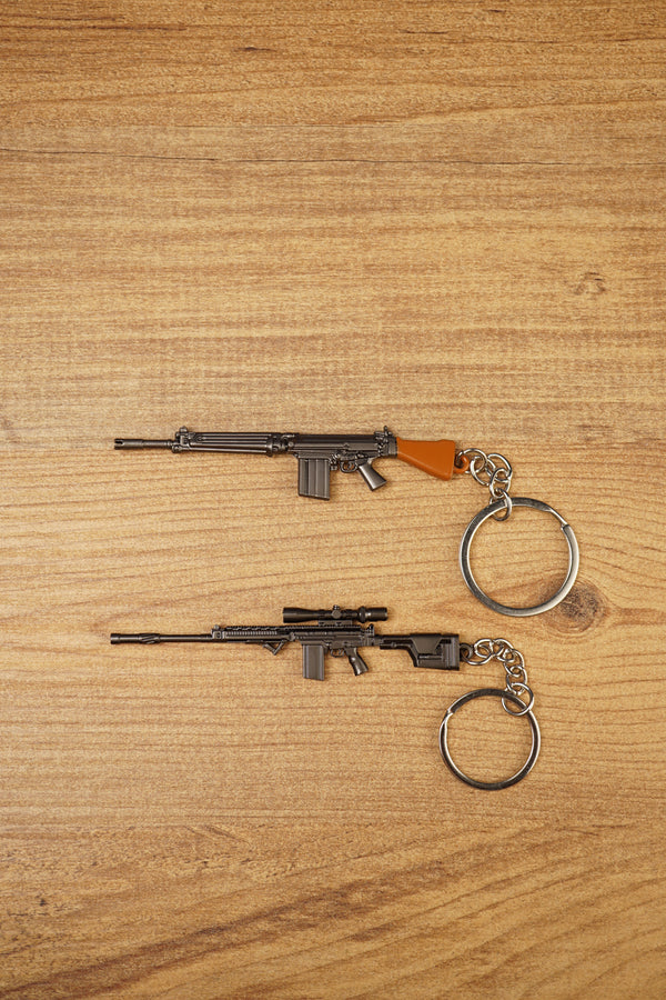 SA58 FAL battle rifle keychains in base and modded styles on a wooden surface, showing metal keyrings and detailed gunmetal finishes
